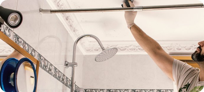 Monteur monteert een douchegordijnrail in een badkamer met douche en tegelwand.