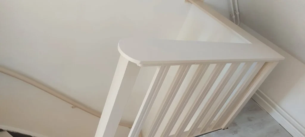 Wit geschilderde houten trapleuning met spijlen langs een binnentrap.