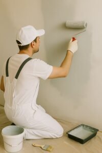 Schilder knielt op de vloer en brengt met een roller een nieuwe verflaag aan op een binnenmuur.