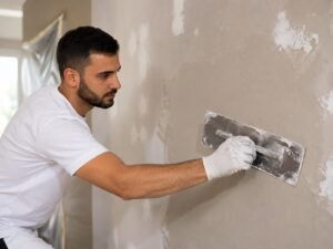 Professionele stukadoor werkt een beschadigde binnenmuur strak af met een pleisterspaan tijdens een renovatieproject.