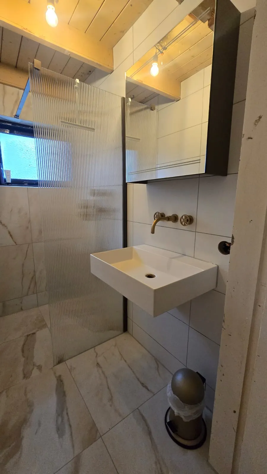 Opgeleverde badkamer met inloopdouche, geribbelde glazen douchewand en marmerlook tegels