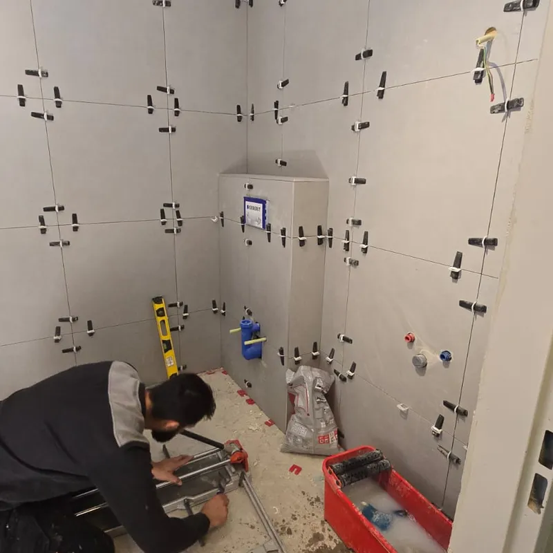 Vakman snijdt wandtegels op maat in een badkamer met een betegelde Geberit voorzetwand