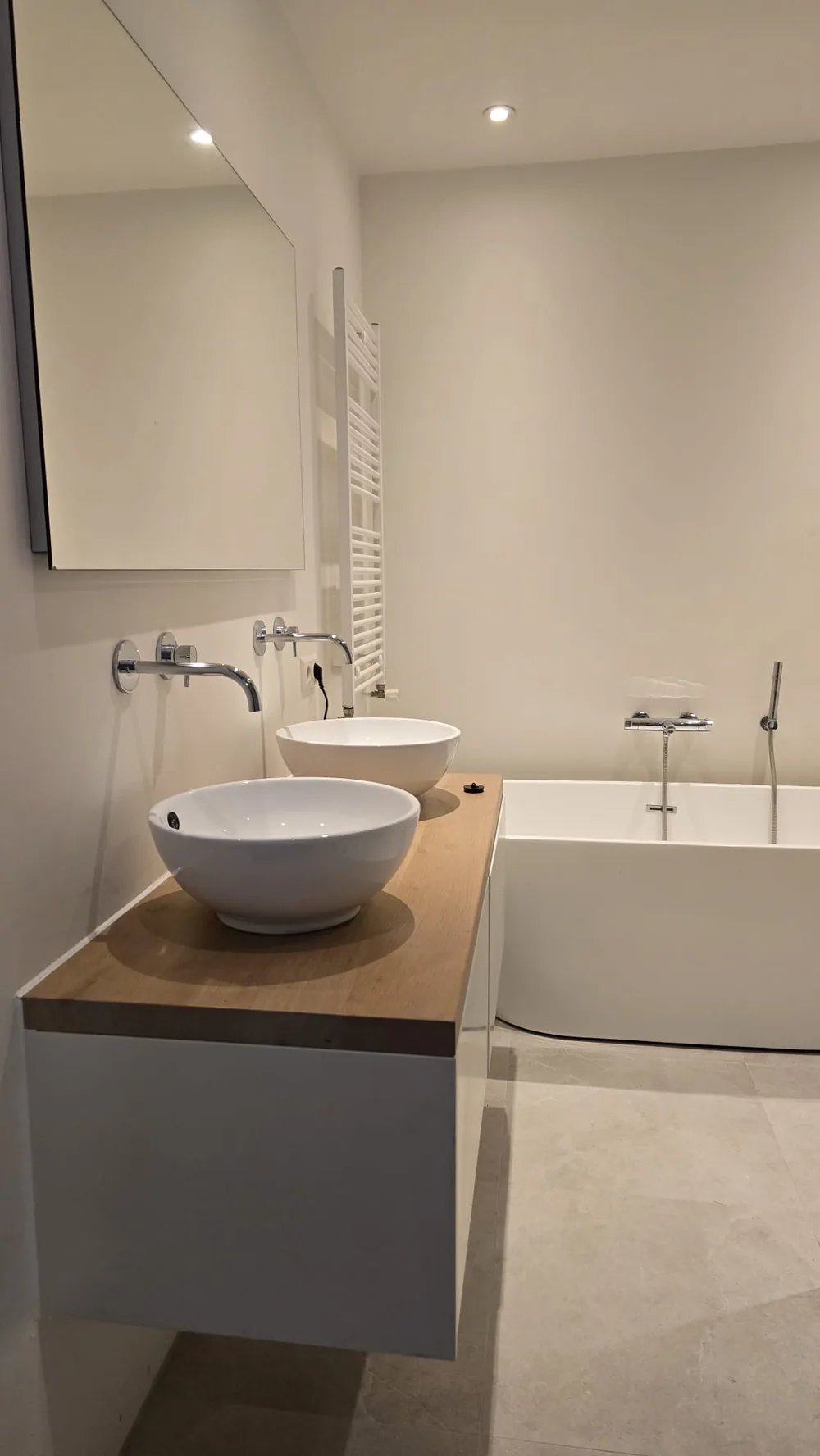 Afgewerkte badkamer met twee waskommen op een eiken wastafelblad en een ligbad