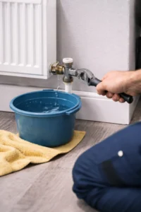 Lekkende radiator waarbij een loodgieter met een sleutel de aansluiting repareert terwijl water in een emmer drupt