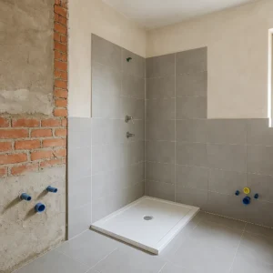 Badkamer in renovatie met nieuw betegelde douchehoek en zichtbare leidingen tegen deels afgewerkte muur.